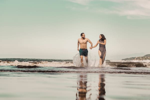 Happy couple holding hands and running through the surf